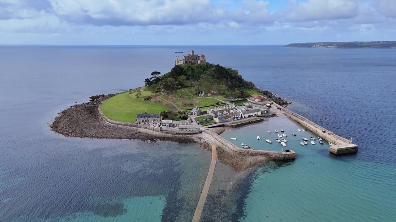Incredibile ripresa aerea con allontanamento e rivelazione di St Michael's Mount e del suo porto, con acque cristalline, strada rialzata soggetta a maree e viste iconiche dell'isola della Cornovaglia