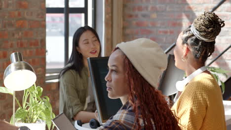 diverse female team collaborating in modern office, discussing coding project with computers
