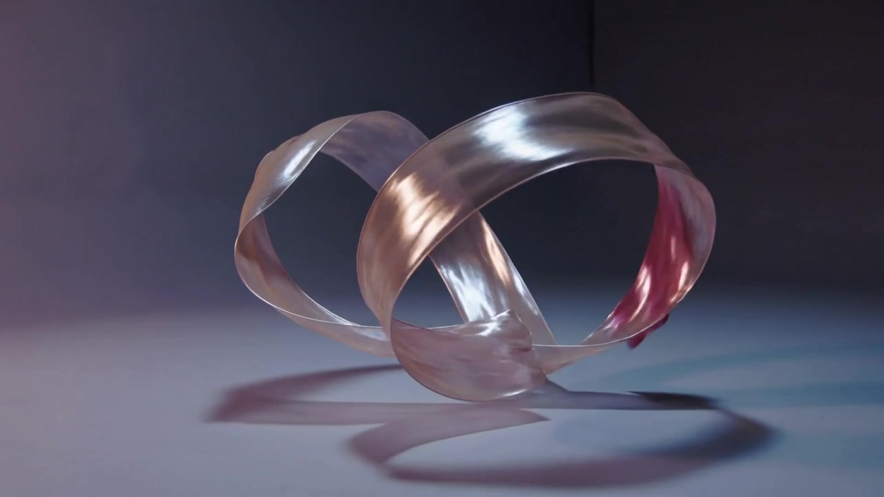 Rotating translucent metallic ribbon curling and settling on studio stage, showing two-tone light