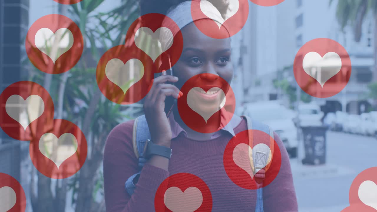 Animation of social media heart icons over smiling african american woman using smartphone in street