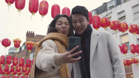 joven pareja asiática de vacaciones posando para selfie en teléfono móvil en chinatown, londres, reino unido 1