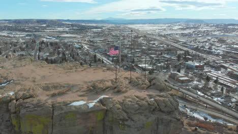 drone view of the us flag waving in the wind on top of a rocky mountain near denver