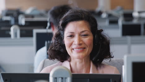 Mature-Businesswoman-Wearing-Telephone-Headset-Talking-To-Caller-In-Customer-Services-Department