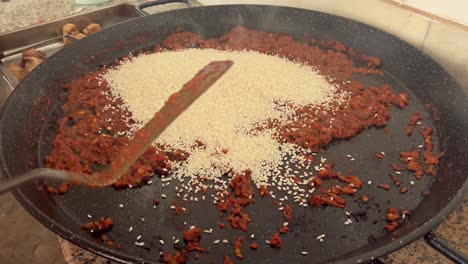 La-Persona-Está-Agregando-Aditivo-Culinario-De-Grano-Blanco-A-Una-Gran-Sartén-De-Metal,-Preparando-Y-Cocinando-El-Concepto-De-Comida