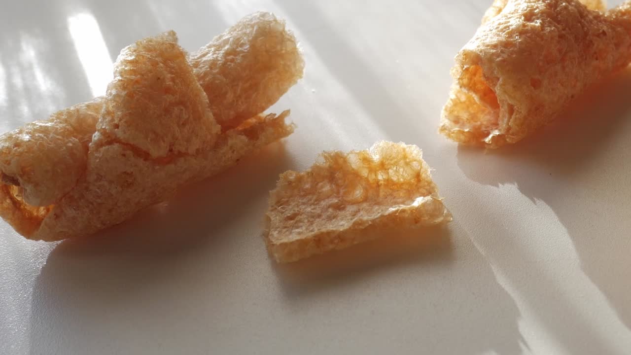 Crispy pork rind pieces on a surface with sunlight highlighting their texture