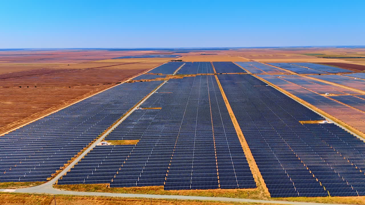 Solar fields produce renewables. Expansive solar panels stretch across a flat landscape under a clear blue sky, showcasing renewable energy production