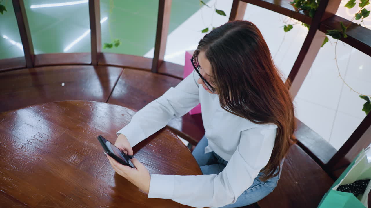 카페 에서 쇼핑 가방 을 들고 친구 와 전화 로 대화 하고 있는 여자 의 위 에서 아래 로 볼 수 있다