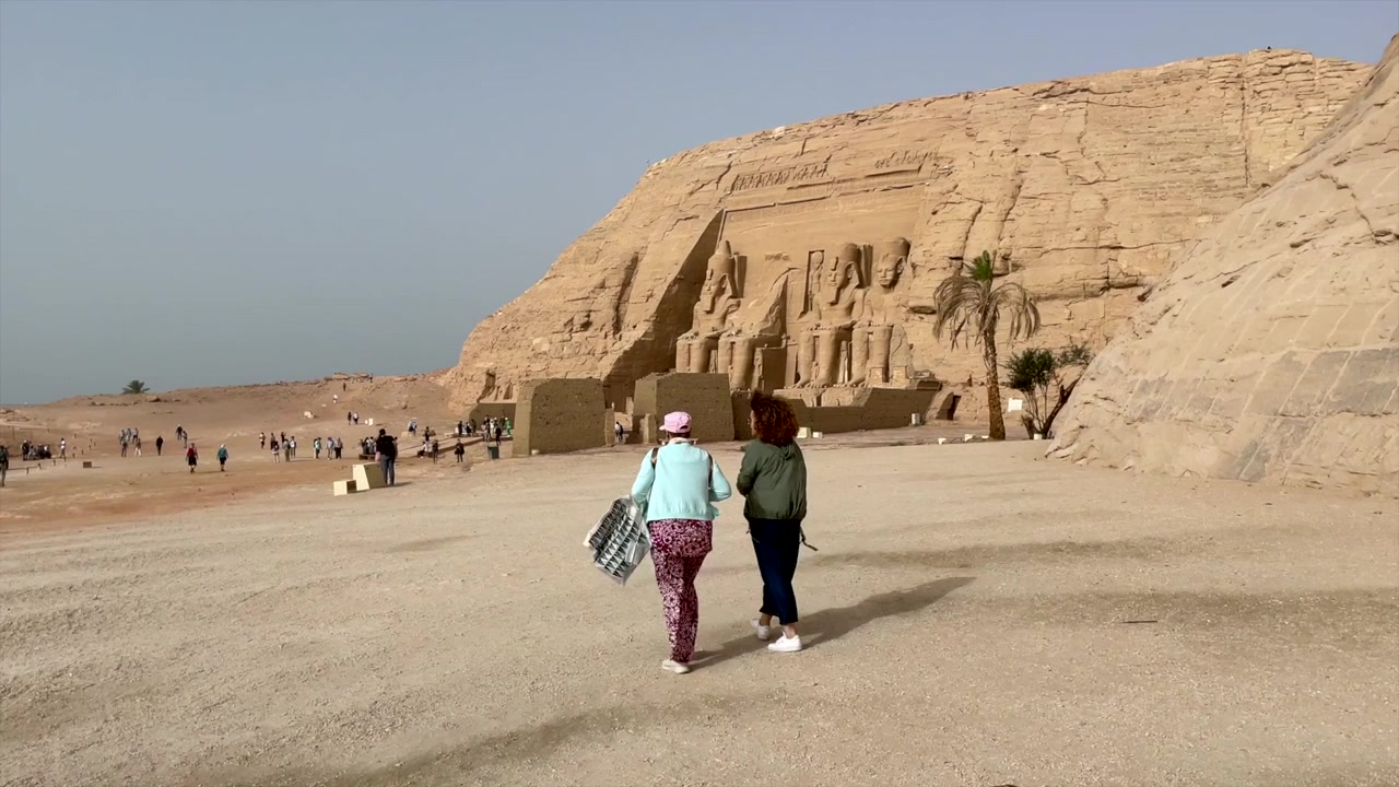 Due turiste anziane camminano verso il tempio di Ramses II ad Abu Simbel. Le viaggiatrici anziane avanzano verso il tempio egizio di Abu Simbel attraverso la superficie desertica in Egitto.