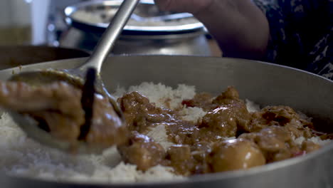 chef adding white rice to layer chicken curry in large pot