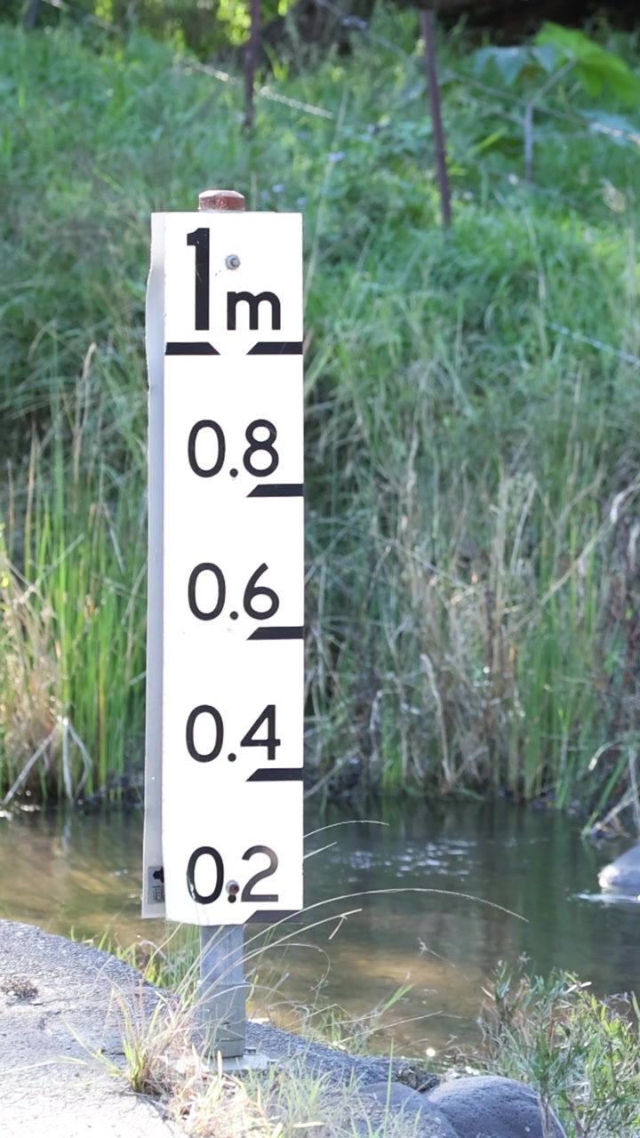 Una ripresa verticale che si concentra su un indicatore bianco di livello dell'acqua accanto a un torrente che scorre.