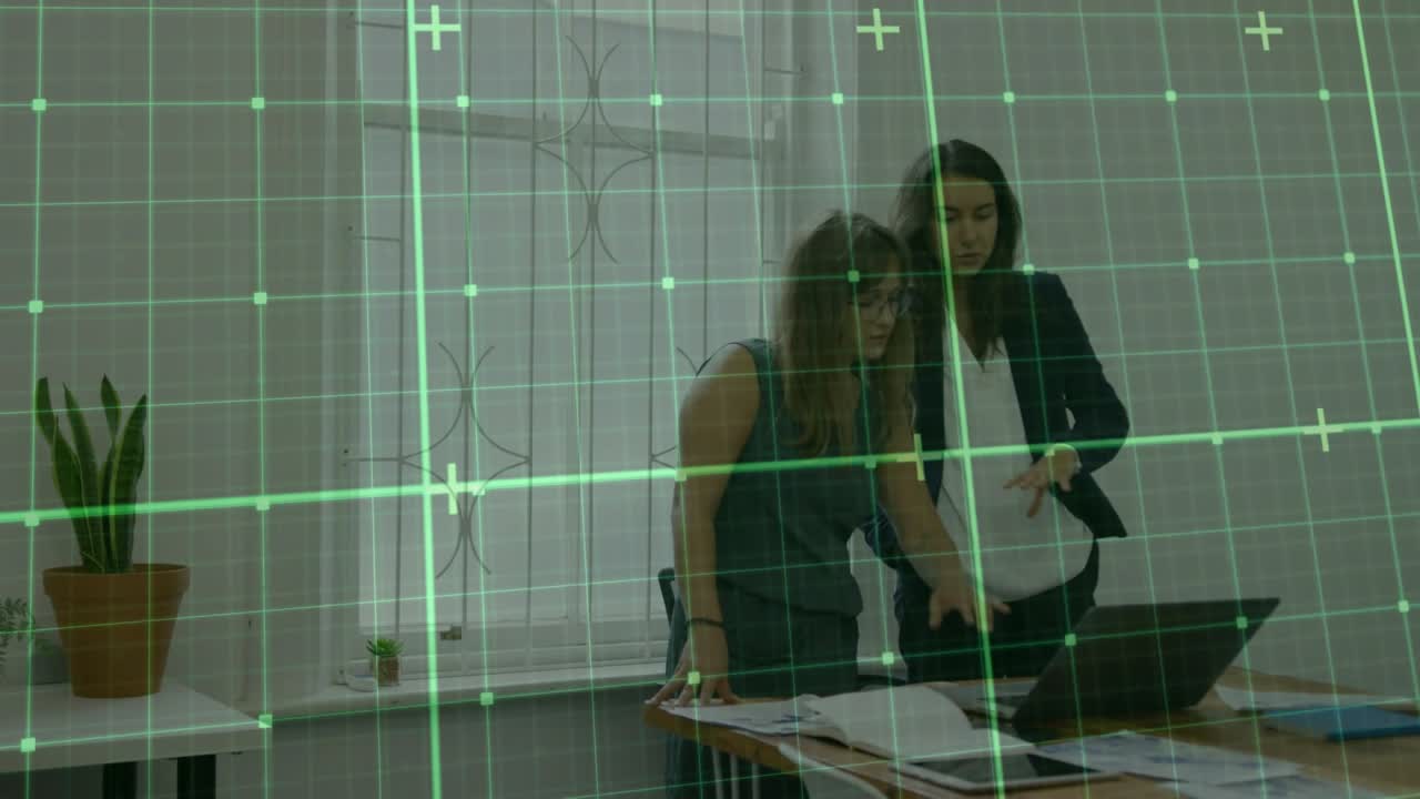 Two colleagues starting design review by inspecting laptop screen and tracing plans over green grid