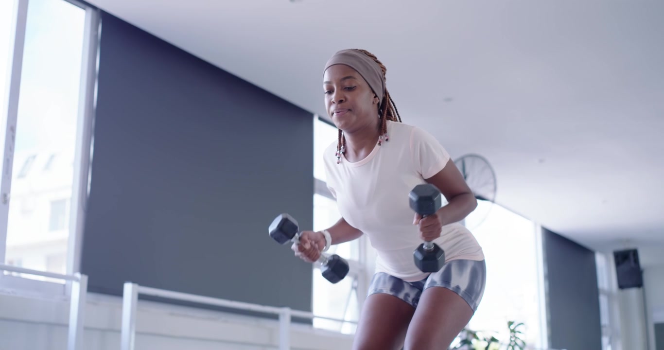 Starting from squat, woman wearing head wrap lifting dumbbells, moving upright, building strength