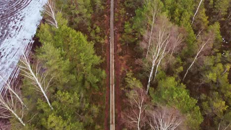 Forest-pathway-with-snow-covered-fields-nearby,-aerial-drone-view