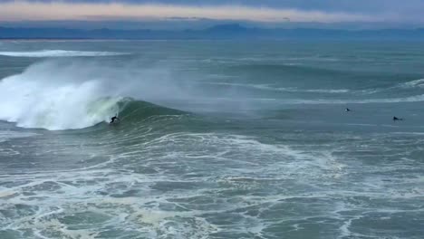 surfer rides a big barreling wave with a jet ski nearby in hossegor, france early morning