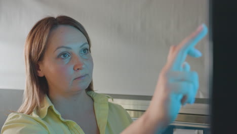 close up face of female entrepreneur at payment kiosk, finger touching screen selecting wash program, focused expression,self service technology, contactless interaction, indoor transaction moment