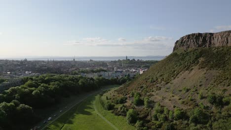 aerial rise at beautiful arthur's seat in holyrood park with edinburgh city centre in the distance, edinburgh, scotland, uk
