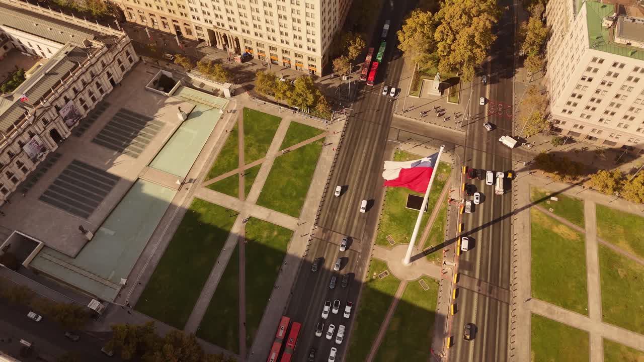 Waving large chilean flag in center of Town. Traffic scene with cars and tram at Bandera Bicentenario In de Chile. Golden sunset time in historic Buildings. Aerial tilt up wide shot.