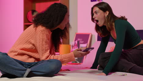 two young women sharing a smartphone on a bed