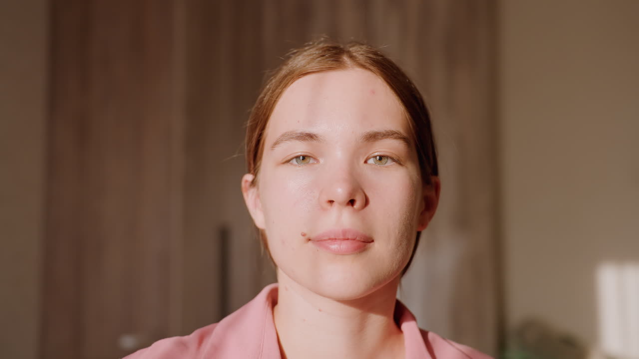 Sunlit Caucasian Woman Wellness Coach Greeting With Sincere Smile And Soft Interior Light, Relaxed Pink Shirt, Curtain Backdrop, Approachable Tone Suited For Telehealth, Selfcare And Lifestyle Content