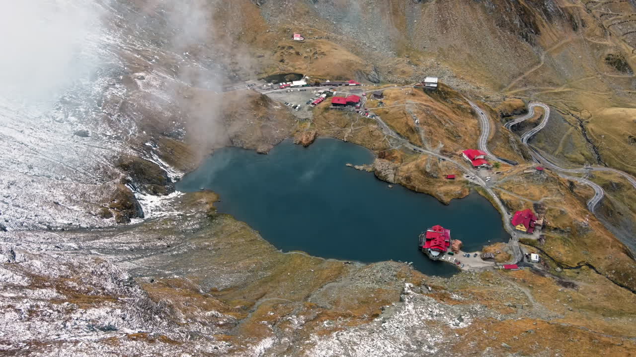 Aerial drone view of nature in Romania. Transfagarasan route in Carpathian mountains, Balea Lake resort and rocky slopes covered with snow, clouds