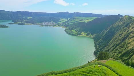 un hermoso valle verde con un lago y colinas exuberantes bajo un cielo azul brillante, vista aérea