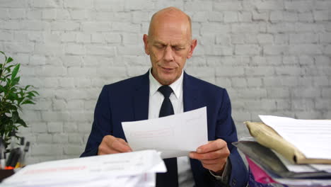 a mature businessman opening a bill envelope at a desk and reading a debt letter with a final notice