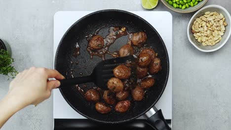 woman cooking meatballs on frying pan with oil