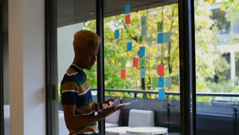 side view of young mixed race male executive looking at sticky note while working on digital tablet