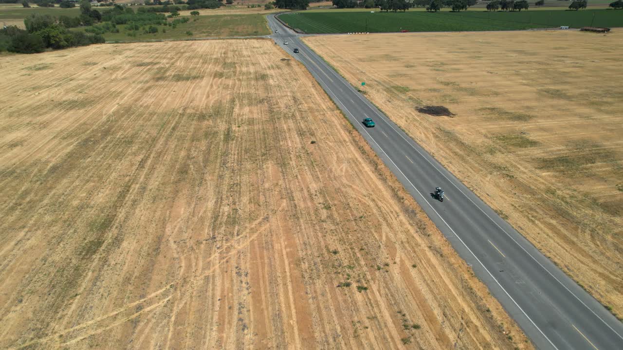 Drone footage of light blue classic mustant driving down rural country roads in California, during the day.