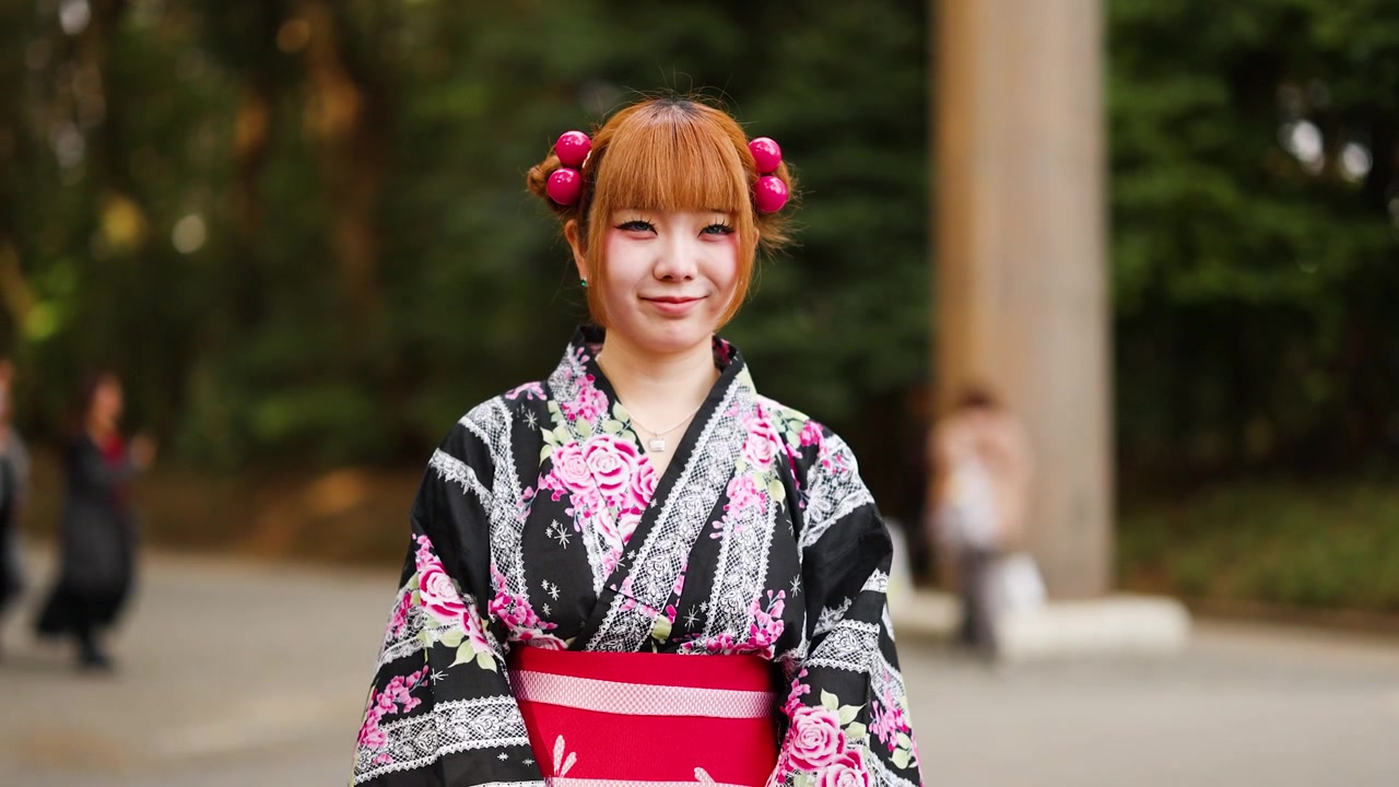 Giovane donna con yukata floreale in piedi davanti a un torii al Santuario Meiji, Tokyo