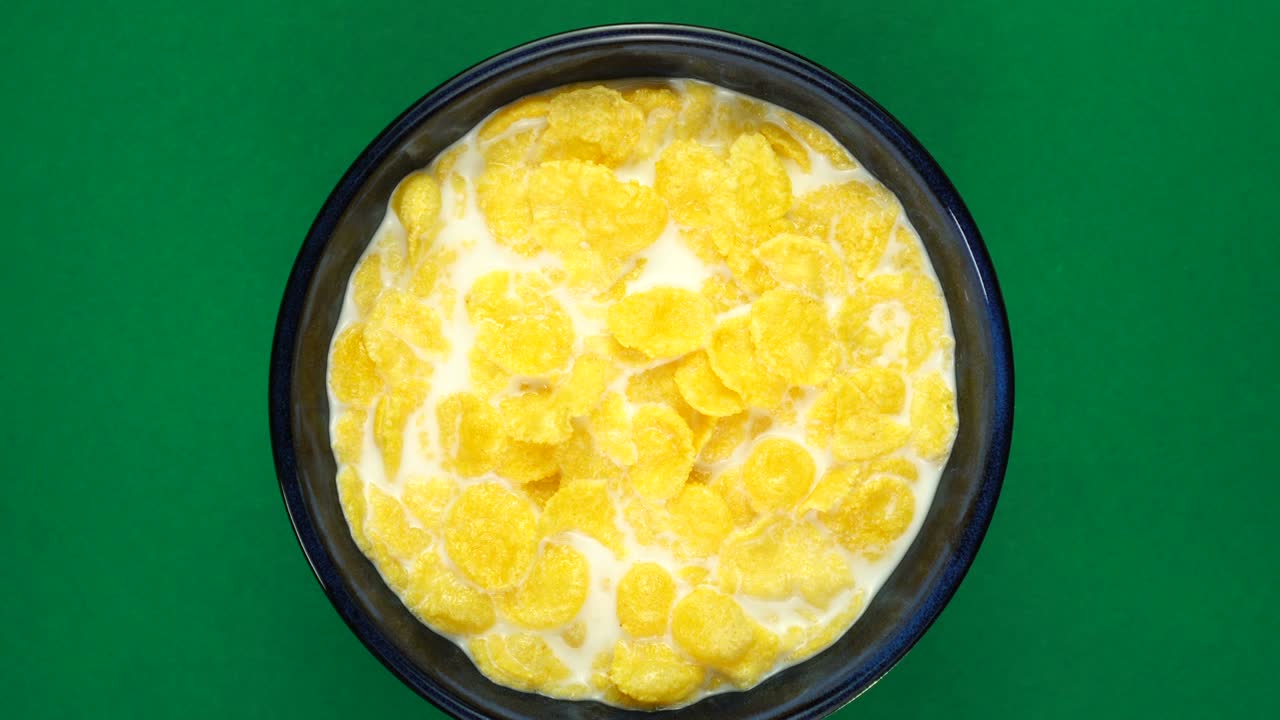 초록색 배경 에 회전 하는 아침 식사 를 위해 우유 에 넣은 황금색 옥수수 어리, 위쪽