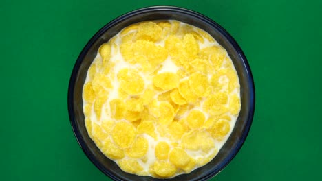 copos de maíz dorados en leche para el desayuno en un fondo verde giratorio, vista de arriba