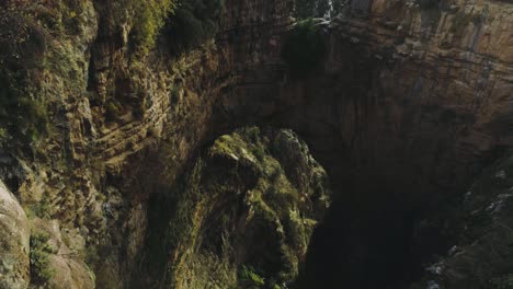 Scenic-view-of-arch-rock-formation-with-man-standing-on-edge-of-cliff,-Lebanon,-circle-pan,-day