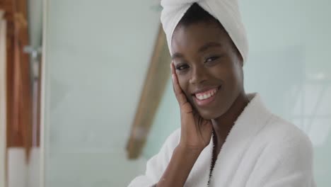 portrait of smiling african american attractive woman wearing robe and turban in bathroom