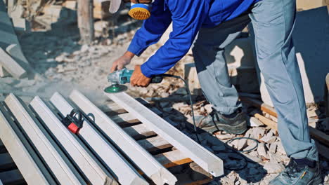 worker is polishing stone by hand grinder outdoors. laborer in working clothes grinding stones on the ground.