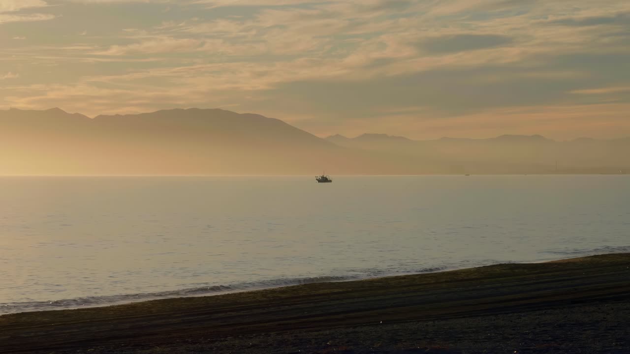silueta de barco de pesca cerca de la playa vacía durante la puesta de sol, con montañas al fondo