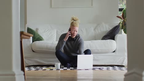 albino african american man with dreadlocks siting on the floor, working and using laptop