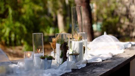 wedding party banquet outdoors in forest. dining table decorated in boho style with candles, white cloth, flowers, served with plates, tableware, dishes, meals, stemware and drinks. holiday catering