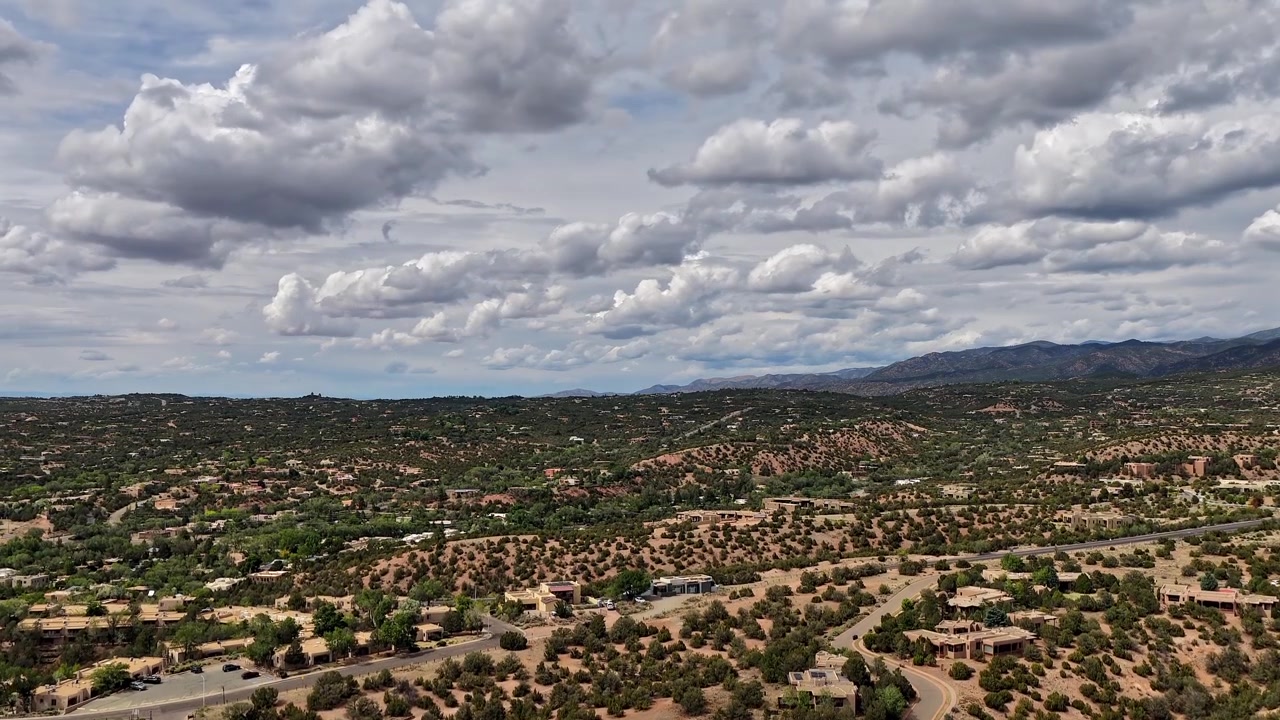 Un delicato timelapse verticale con drone che si eleva sulle pendici settentrionali di Santa Fe, Nuovo Messico. Strati nuvolosi stratificati che si muovono fluttuano sopra la vasta topografia suburbana e le colline aspre