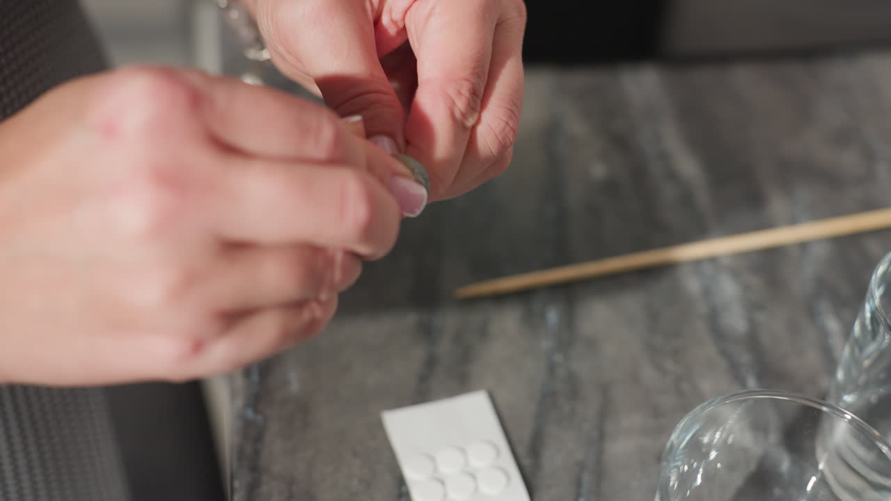 close up hand view of person preparing for beads design with tools on marble countertop, holding components carefully with manicured nails, background includes sticks, glass, and design materials