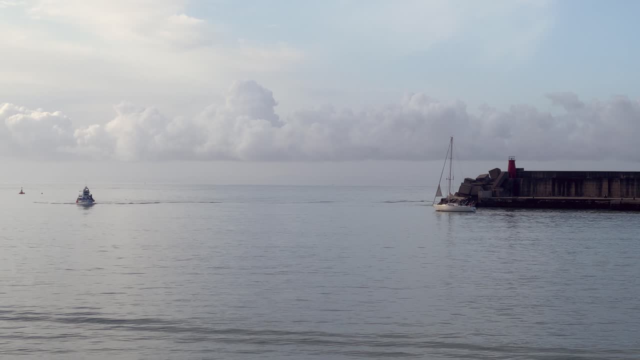 Static view of a sailboat and speedboat sailing near marina. Daylight