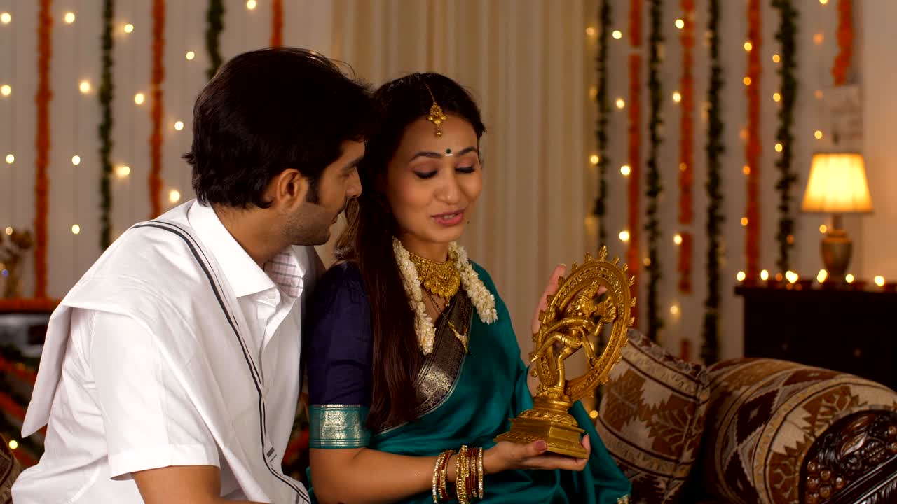 Beautifully dressed woman with her husband - Holding a statue of Lord Nataraja with a festive background