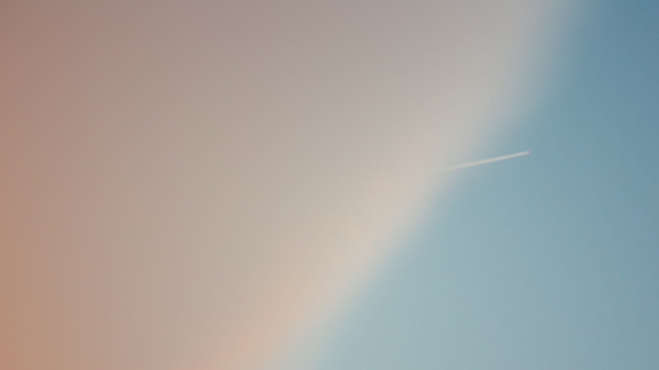 Minimalist image of soft pink cloud meeting blue sky with faint airplane trail