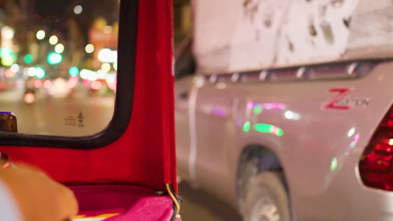 Point-of-view tuk tuk ride through colorful night traffic with neon lights and soft bokeh