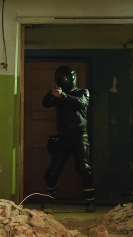 person in leather moto costume with helmet holds handgun coming into room with piles of garbage in old abandoned building slow motion