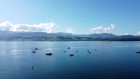 Snowdonia-clear-mountain-range-aerial-view-sunny-calm-Welsh-shimmering-seascape-panning-left-across-landscape