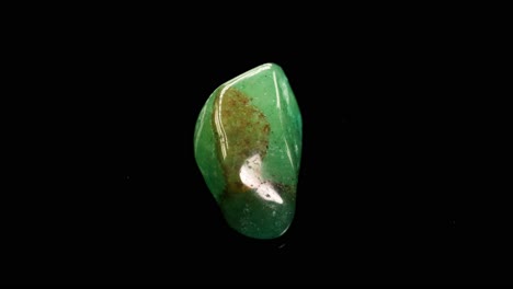 green aventurine stones rotate against a black background, highlighting their glossy texture and natural patterns under soft lighting