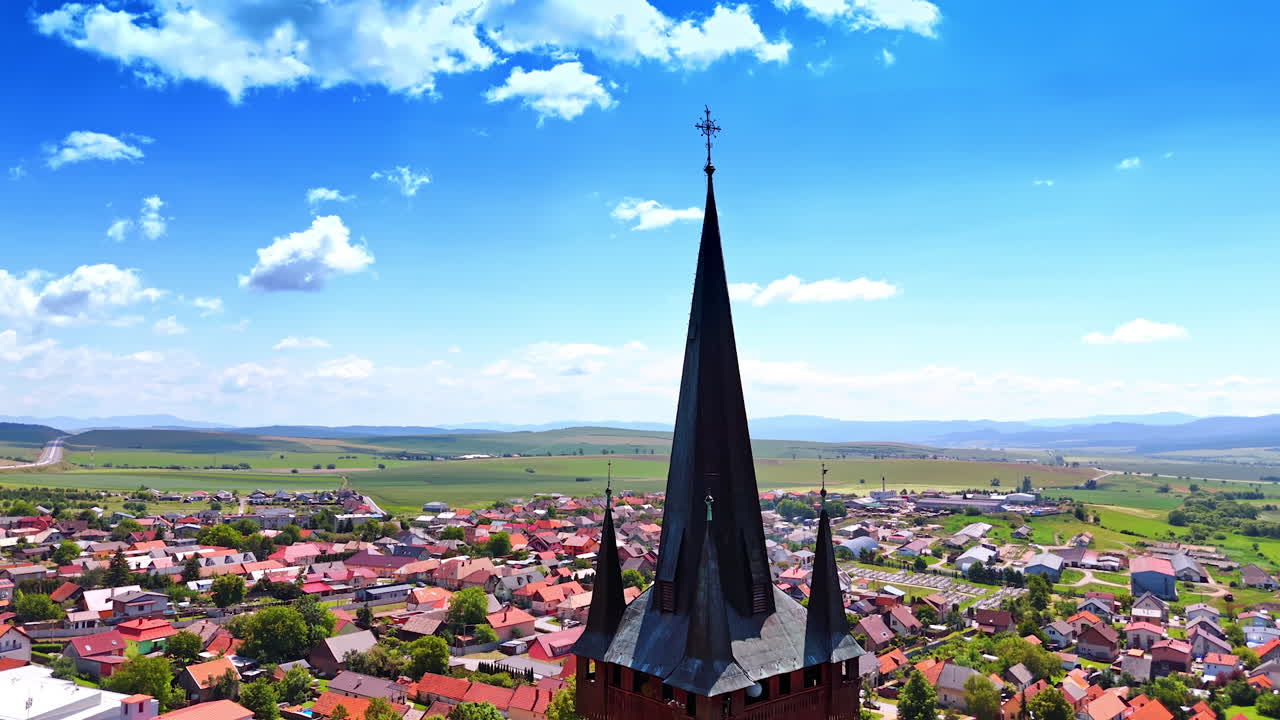 Scenic view of town with church steeple. Bright day showcasing a church steeple overlooking a vibrant town surrounded by green fields and distant mountains