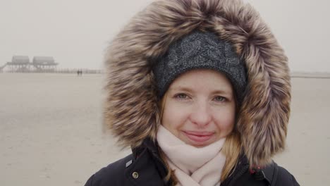 young woman standing in the wind of a barren landscape, protected from the freezing cold with a fur hood - facing camera