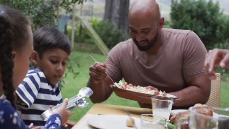 Happy-biracial-parents,-son-and-daughter-enjoying-meal-at-dinner-table-in-garden,-slow-motion